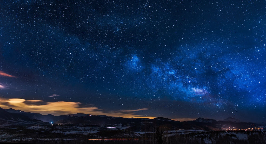 A star-filled night sky above dark mountain silhouettes